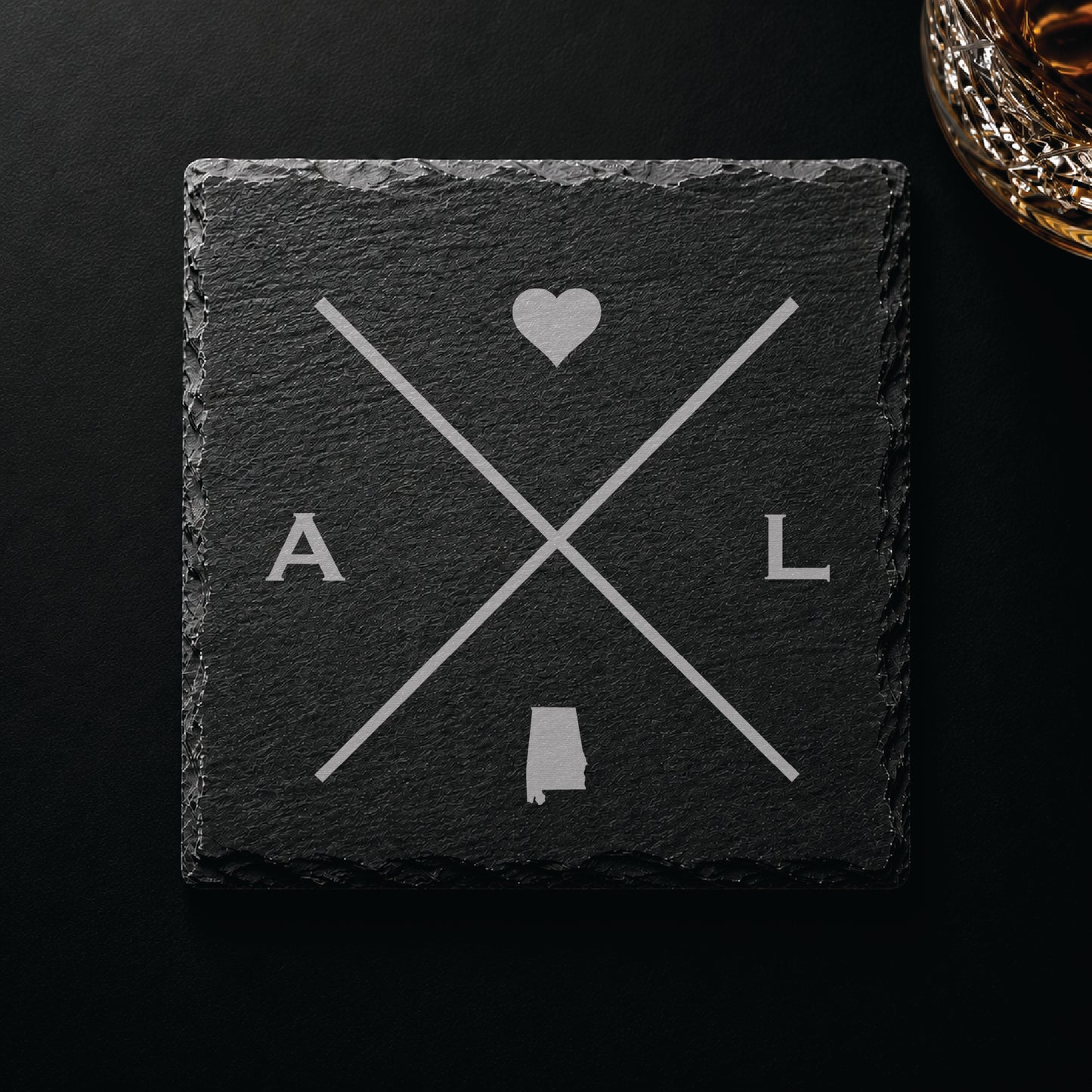 Dark slate coaster with engraved Alabama crossed-line design, heart icon, and Alabama silhouette on a dark background.