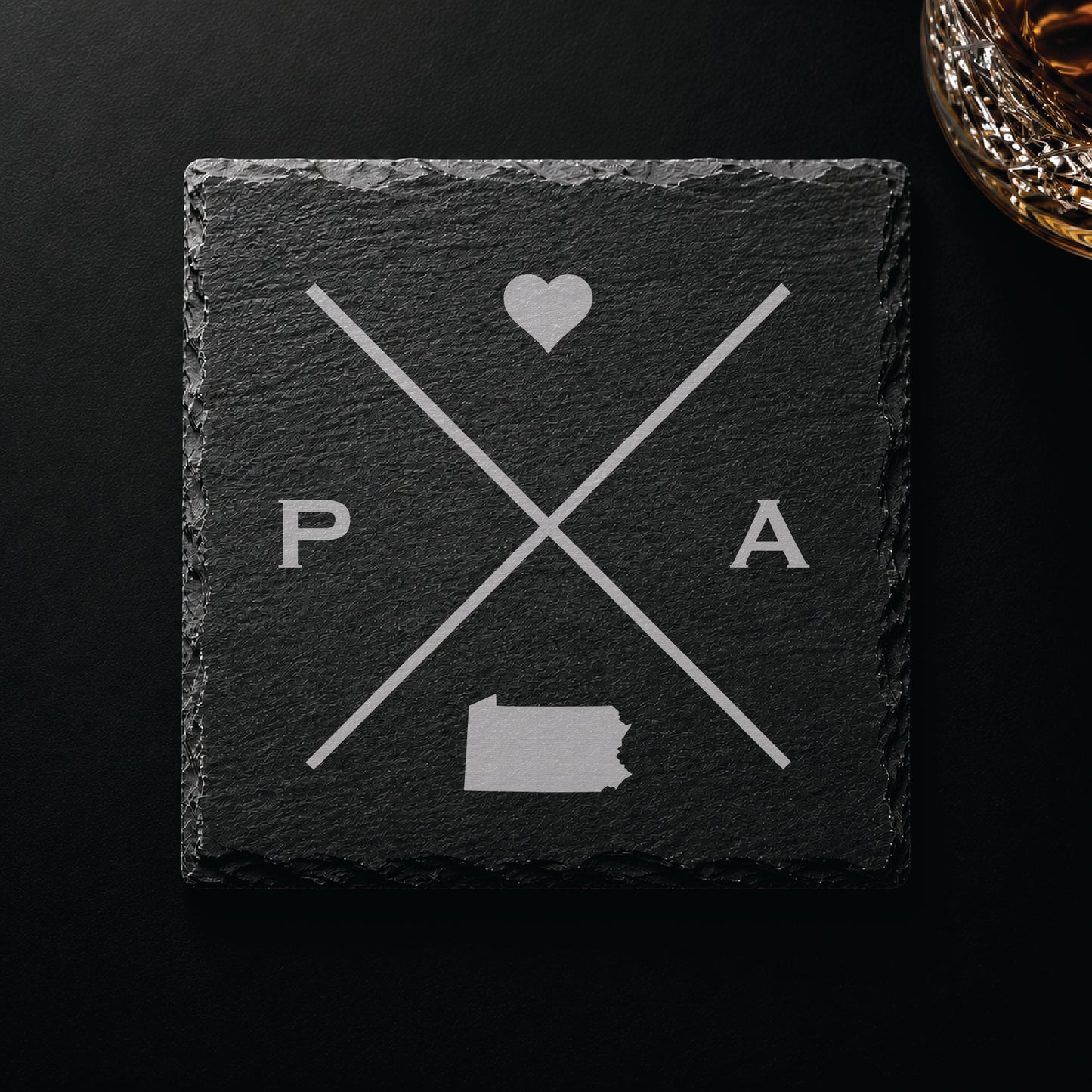 Dark slate coaster with engraved Pennsylvania crossed-line design, heart icon, and Pennsylvania silhouette on a dark background.