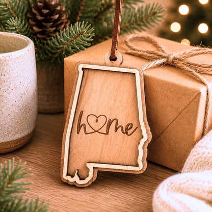 Layered Alabama wood ornament with engraved “home” script displayed beside wrapped holiday gifts, greenery, and warm seasonal décor.