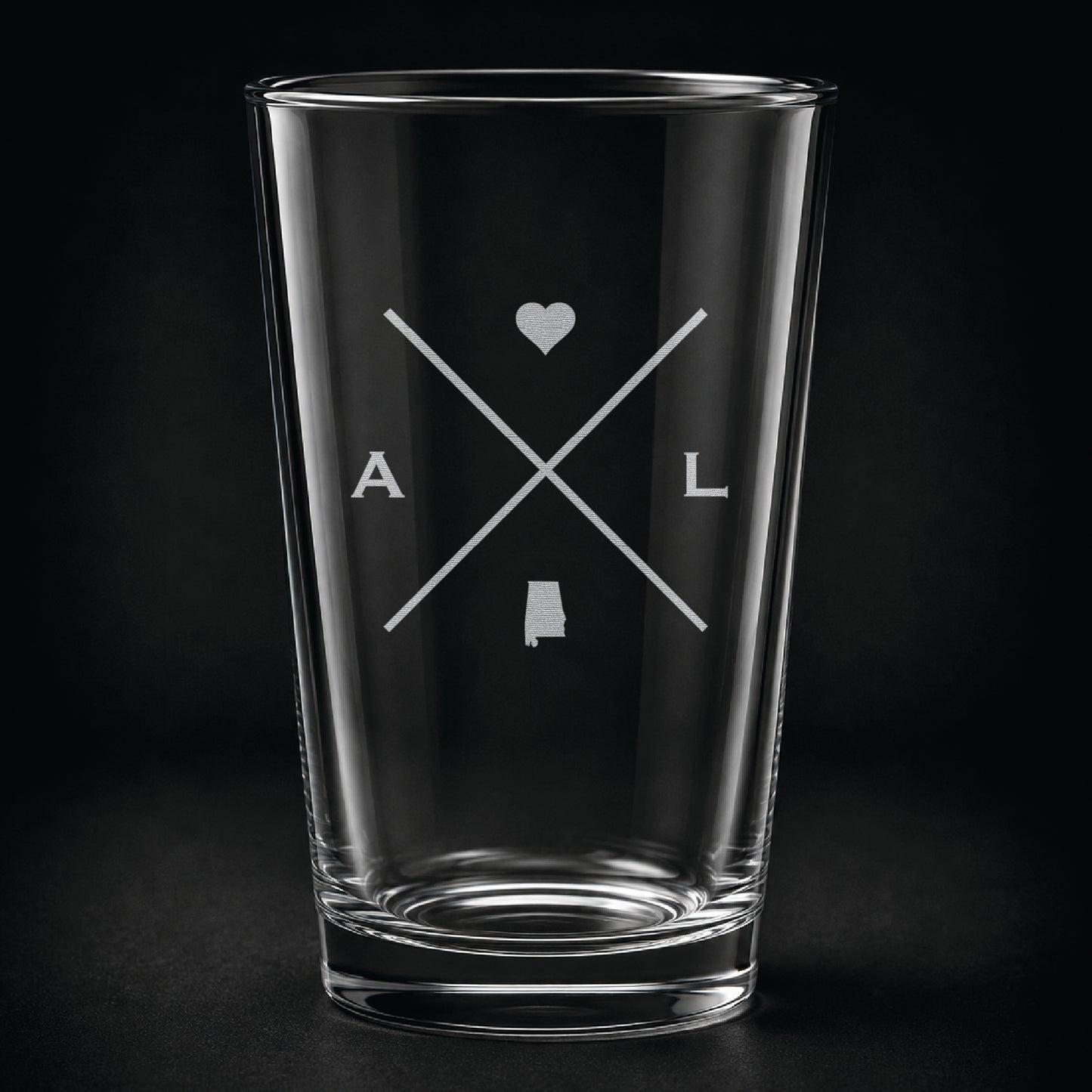 Engraved Alabama pint glass featuring a minimalist crossed-line design with heart detail and Alabama silhouette on a dark background.