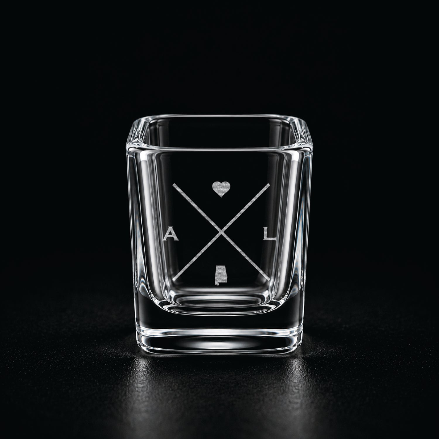 Engraved Alabama shot glass with modern crossed-line state design and frosted laser engraving on a dark background.