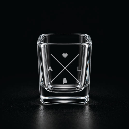 Engraved Alabama shot glass with modern crossed-line state design and frosted laser engraving on a dark background.