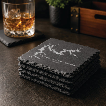 Stack of engraved Lake Allatoona slate coasters in a warm bar-style setting with whiskey glass nearby, featuring a detailed lake map design and Georgia text.
