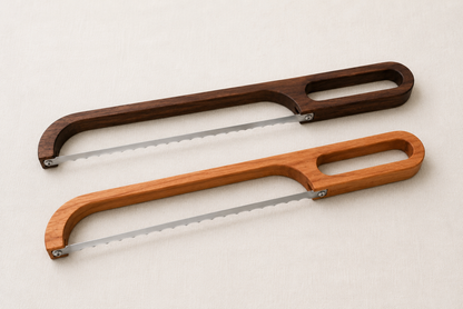 Minimal studio comparison image of walnut and cherry bread bow knives displayed side by side on a neutral fabric background.