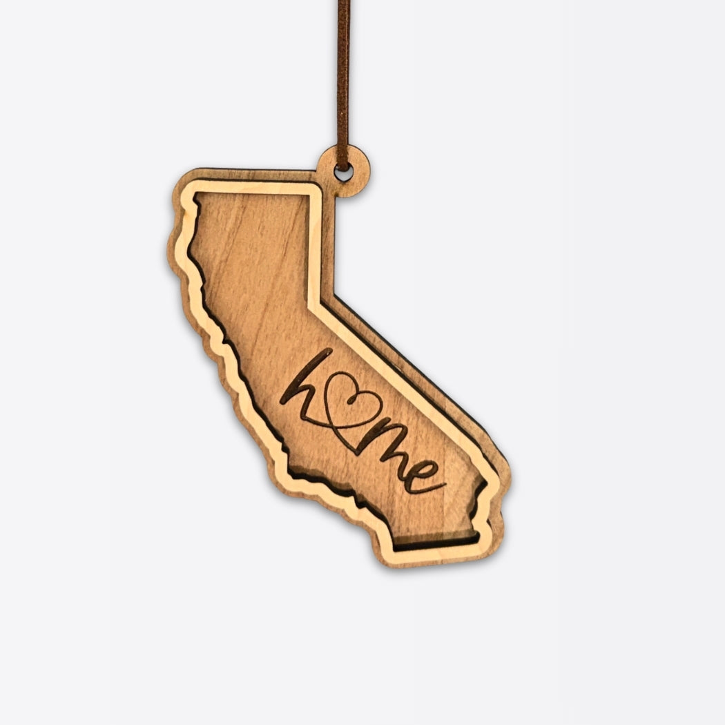 Layered California wood ornament with engraved “home” script and faux leather cord on white background.