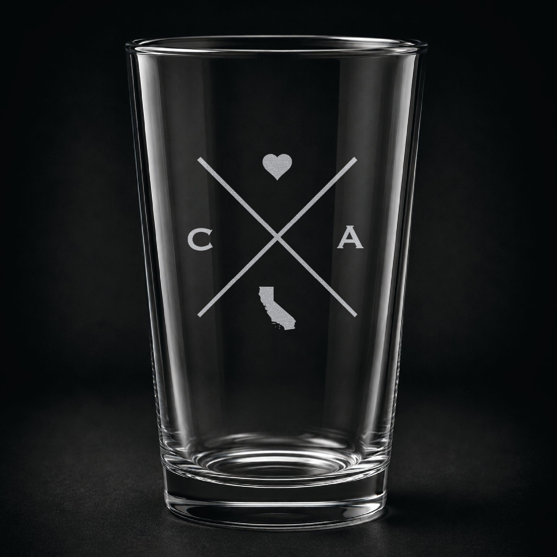 Engraved California pint glass featuring a minimalist crossed-line design with heart detail and California silhouette on a dark background.