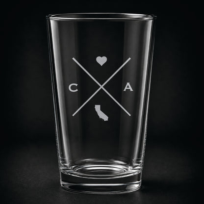 Engraved California pint glass featuring a minimalist crossed-line design with heart detail and California silhouette on a dark background.
