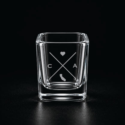 Engraved California shot glass with modern crossed-line state design and frosted laser engraving on a dark background.