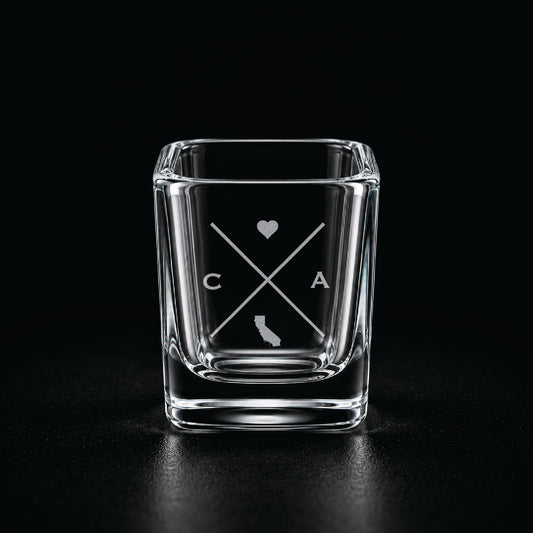 Engraved California shot glass with modern crossed-line state design and frosted laser engraving on a dark background.
