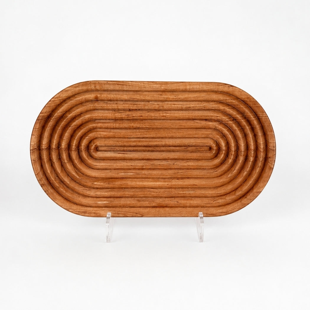 Cherry wood bread board on white background with fluted carved detailing, rounded raised ridges, and warm cherry wood grain displayed on a clear acrylic stand.