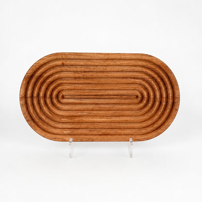 Cherry wood bread board on white background with fluted carved detailing, rounded raised ridges, and warm cherry wood grain displayed on a clear acrylic stand.