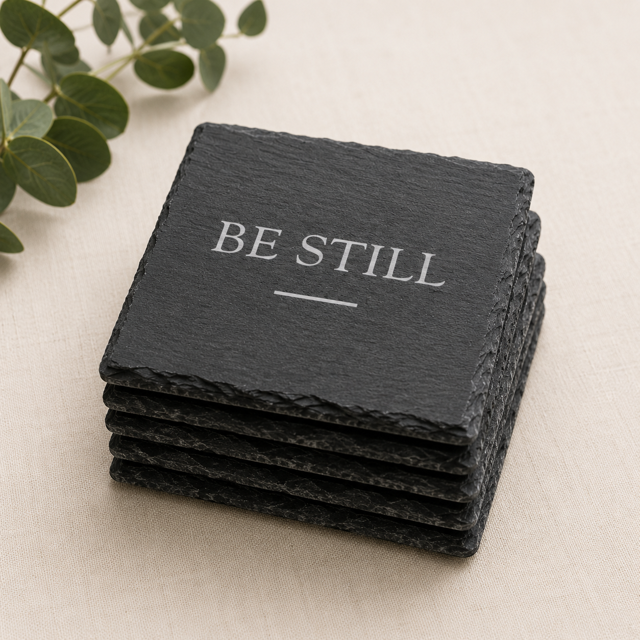 Stack of black slate coasters with 'BE STILL' text on a light background