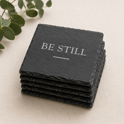 Stack of black slate coasters with 'BE STILL' text on a light background