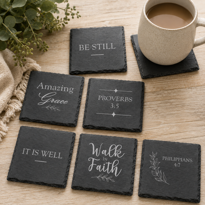 Engraved Christian slate coasters displayed on a wooden tabletop with a ceramic coffee mug and eucalyptus greenery in a cozy home setting.