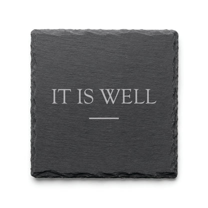 Black slate coaster engraved with the phrase It Is Well and a simple decorative line.