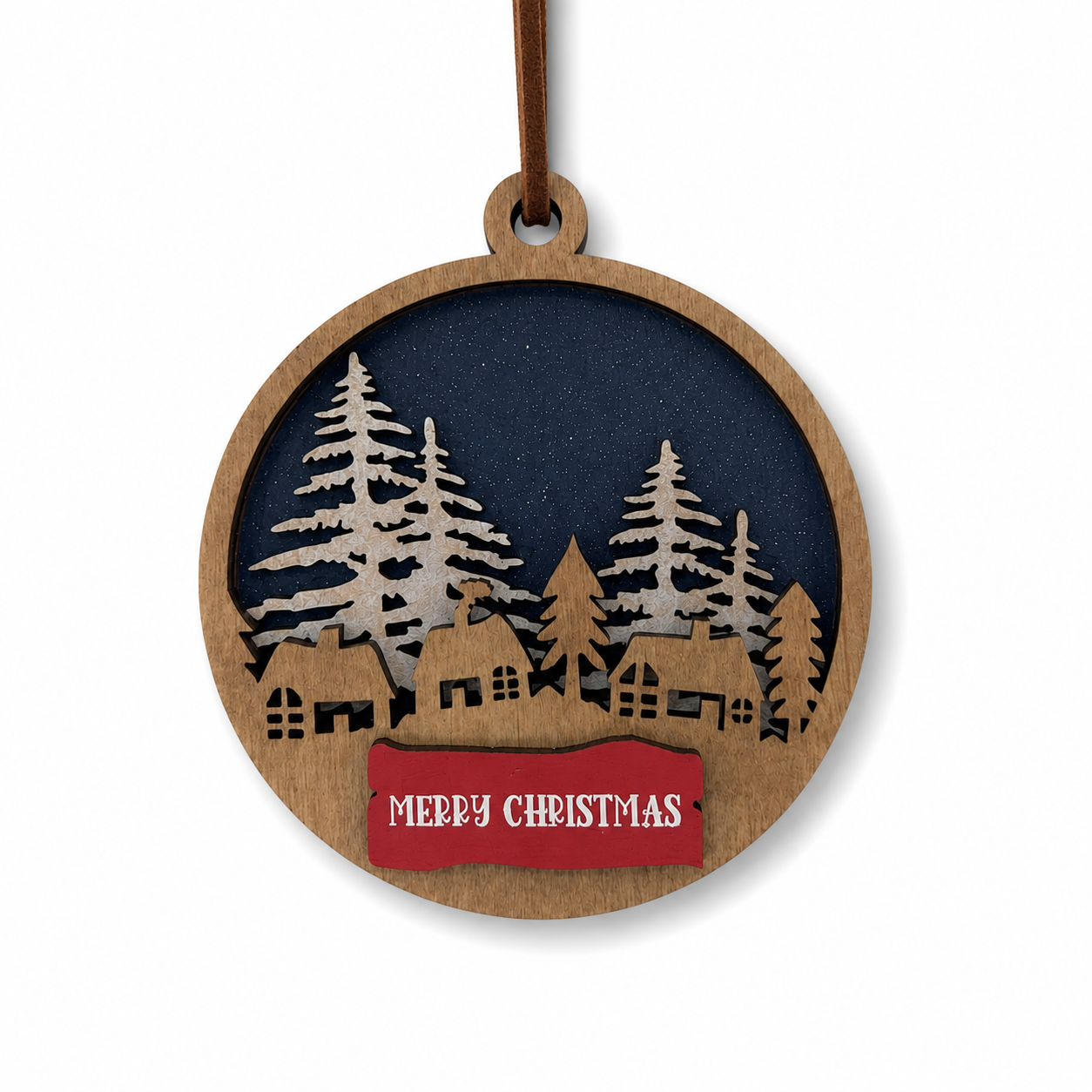 Layered Christmas village ornament with woodland cabins, pine trees, blue night sky, and red Merry Christmas banner on a clean white background