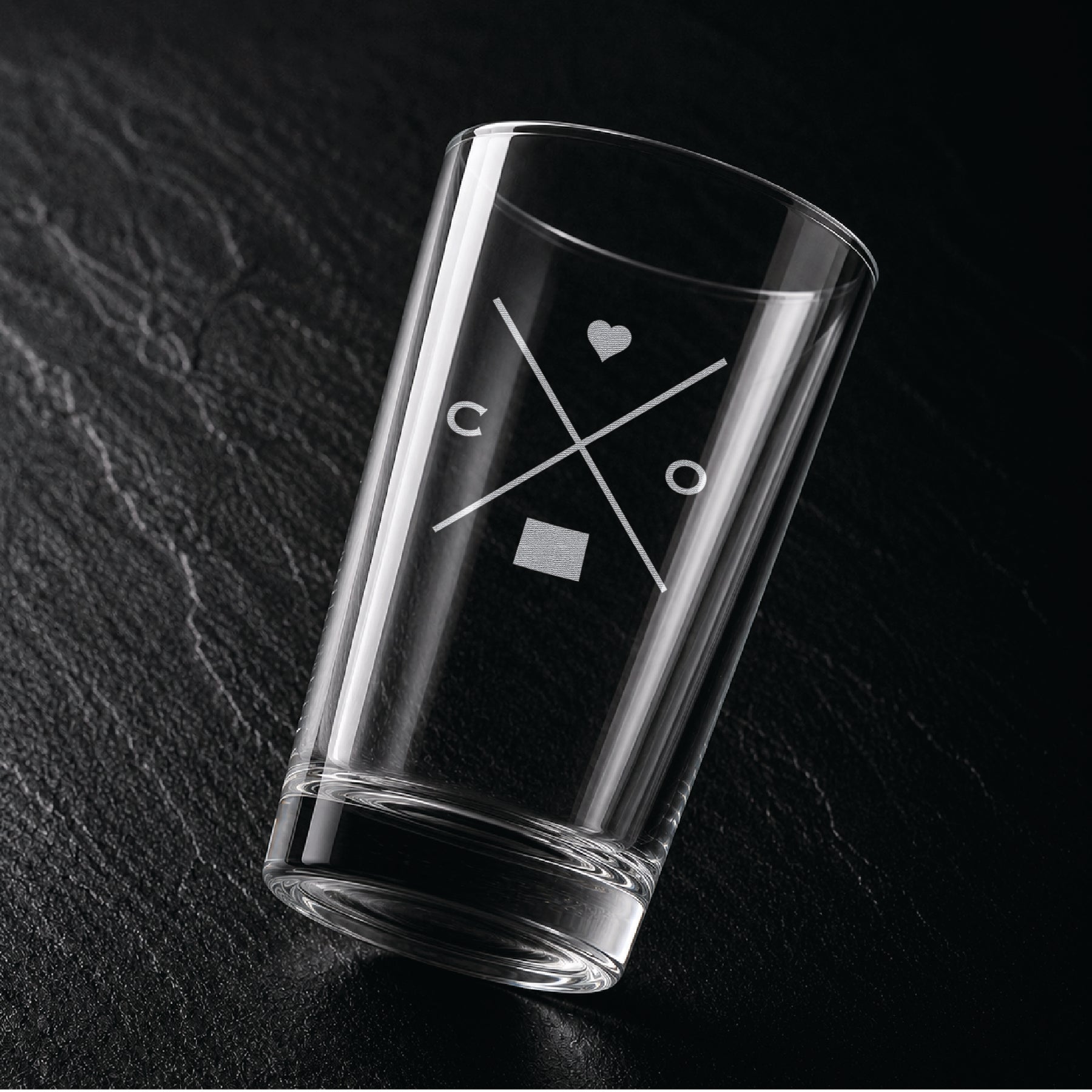 Angled view of engraved Colorado pint glass with modern crossed-line state design and frosted laser engraving on dark textured surface.