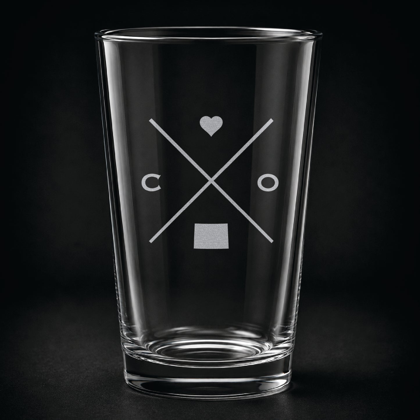 Engraved Colorado pint glass featuring a minimalist crossed-line design with heart detail and Colorado silhouette on a dark background.