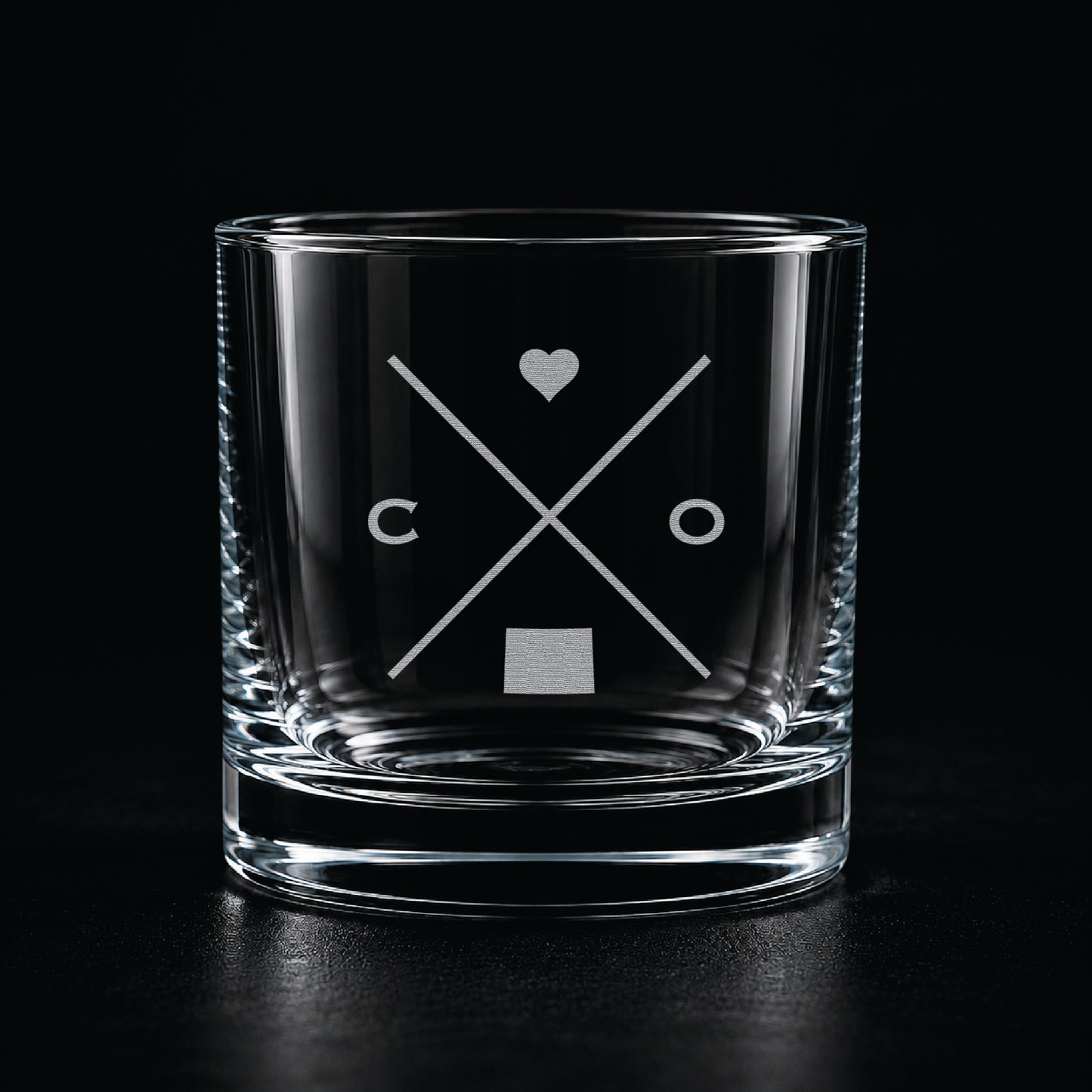Engraved Colorado rocks glass with frosted Colorado silhouette and crossed-letter monogram on a dark background.