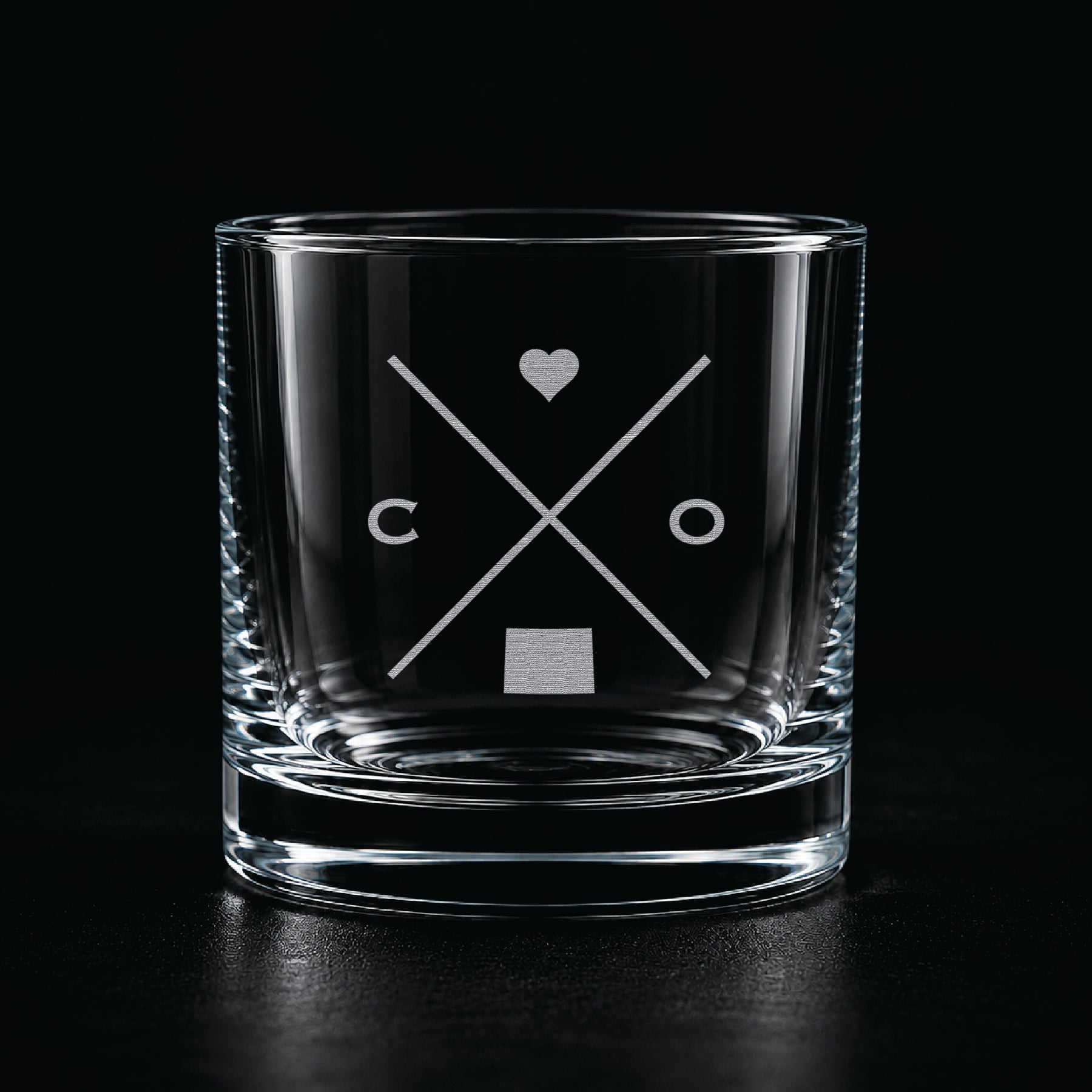 Engraved Colorado rocks glass with frosted Colorado silhouette and crossed-letter monogram on a dark background.
