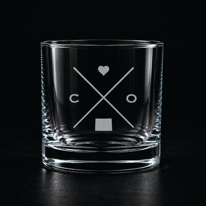 Engraved Colorado rocks glass with frosted Colorado silhouette and crossed-letter monogram on a dark background.