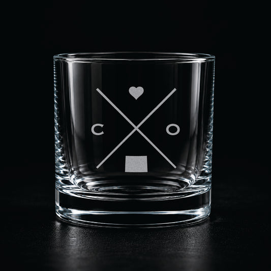 Engraved Colorado rocks glass with frosted Colorado silhouette and crossed-letter monogram on a dark background.