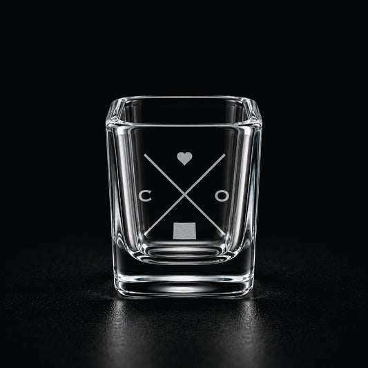 Engraved Colorado shot glass with modern crossed-line state design and frosted laser engraving on a dark background.