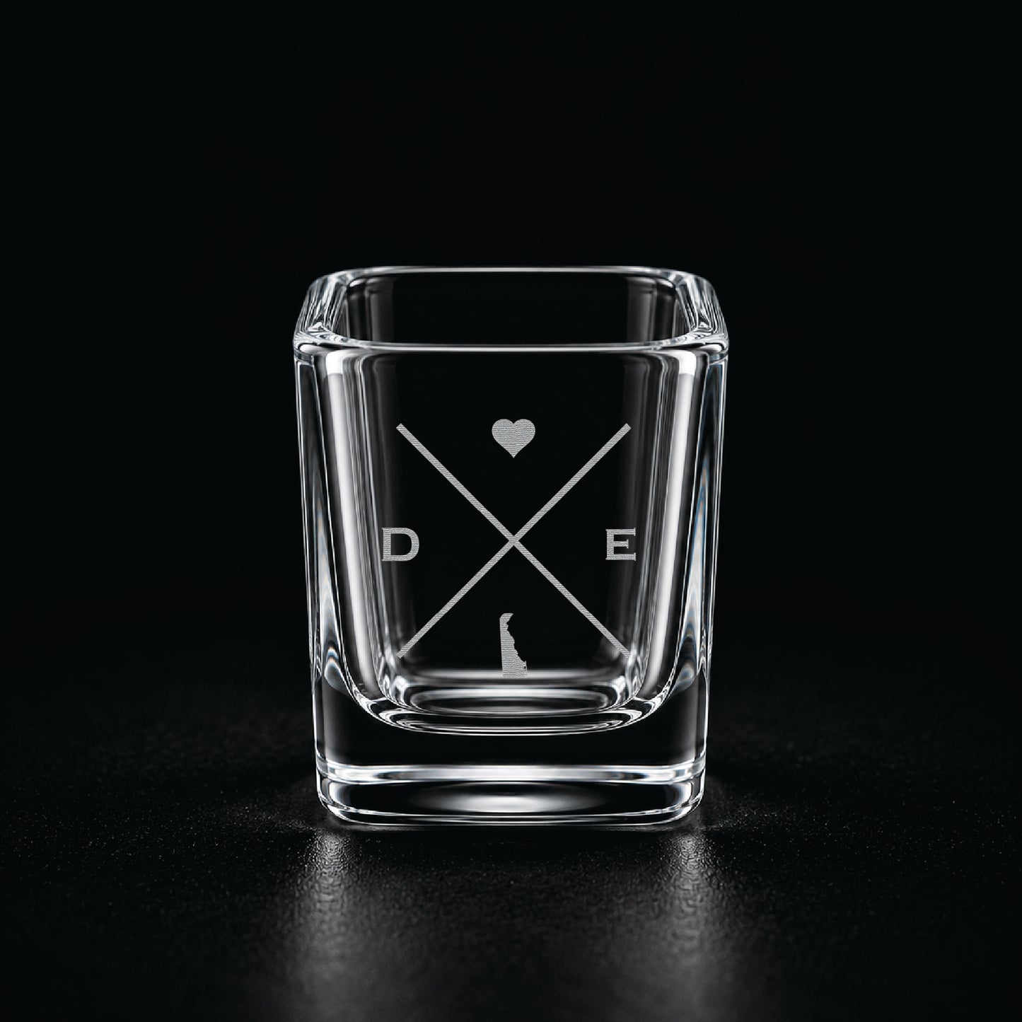 Engraved Delaware shot glass with modern crossed-line state design and frosted laser engraving on a dark background.