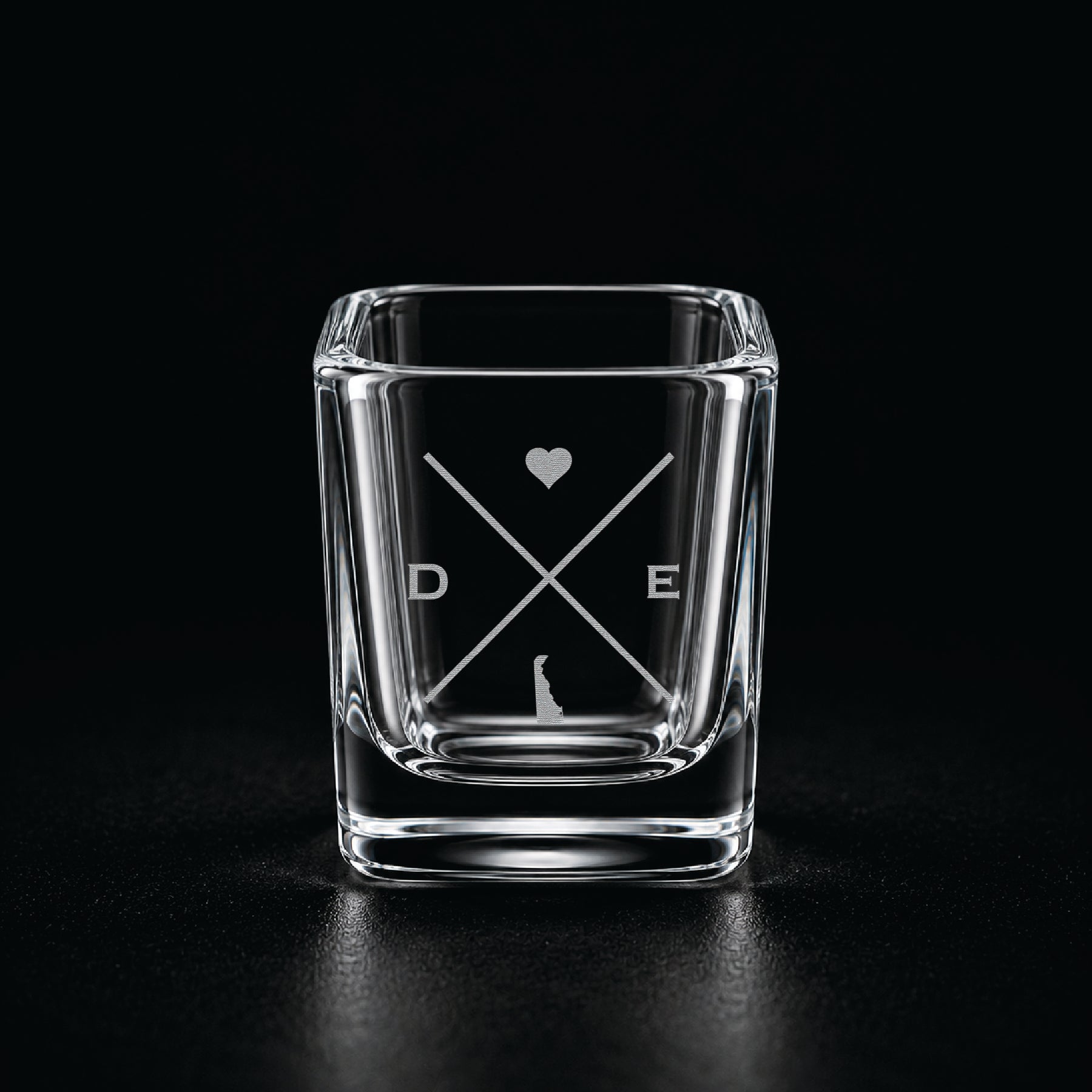 Engraved Delaware shot glass with modern crossed-line state design and frosted laser engraving on a dark background.