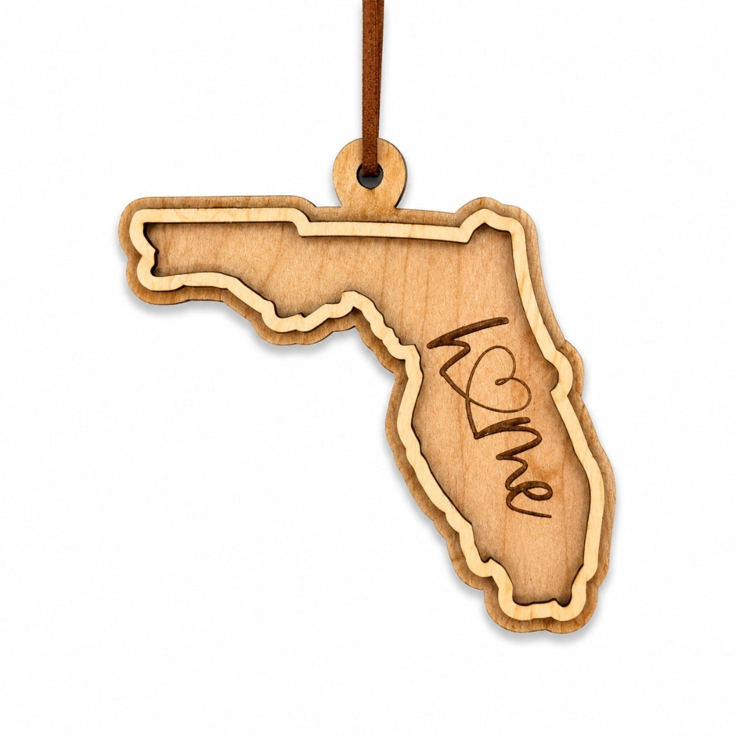 Layered Florida wood ornament with engraved “home” script and faux leather cord on white background.