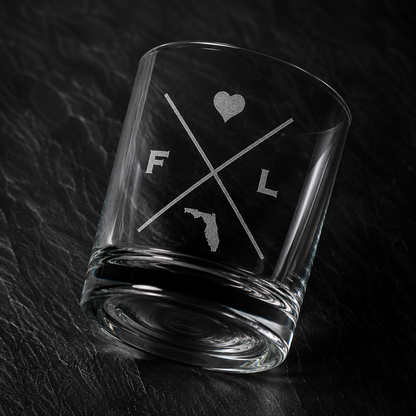 Angled engraved Florida whiskey glass featuring frosted Florida silhouette and modern crossed-letter design on a dark textured surface.