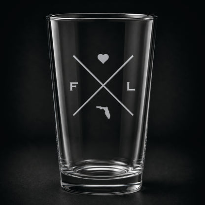 Engraved Florida pint glass featuring a minimalist crossed-line design with heart detail and Florida silhouette on a dark background.