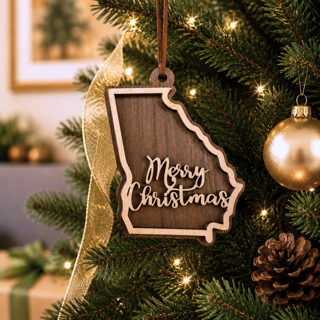 Layered Georgia state Christmas ornament hanging on a decorated Christmas tree, featuring walnut and maple wood tones, “Merry Christmas” script, warm white lights, and neutral festive décor.