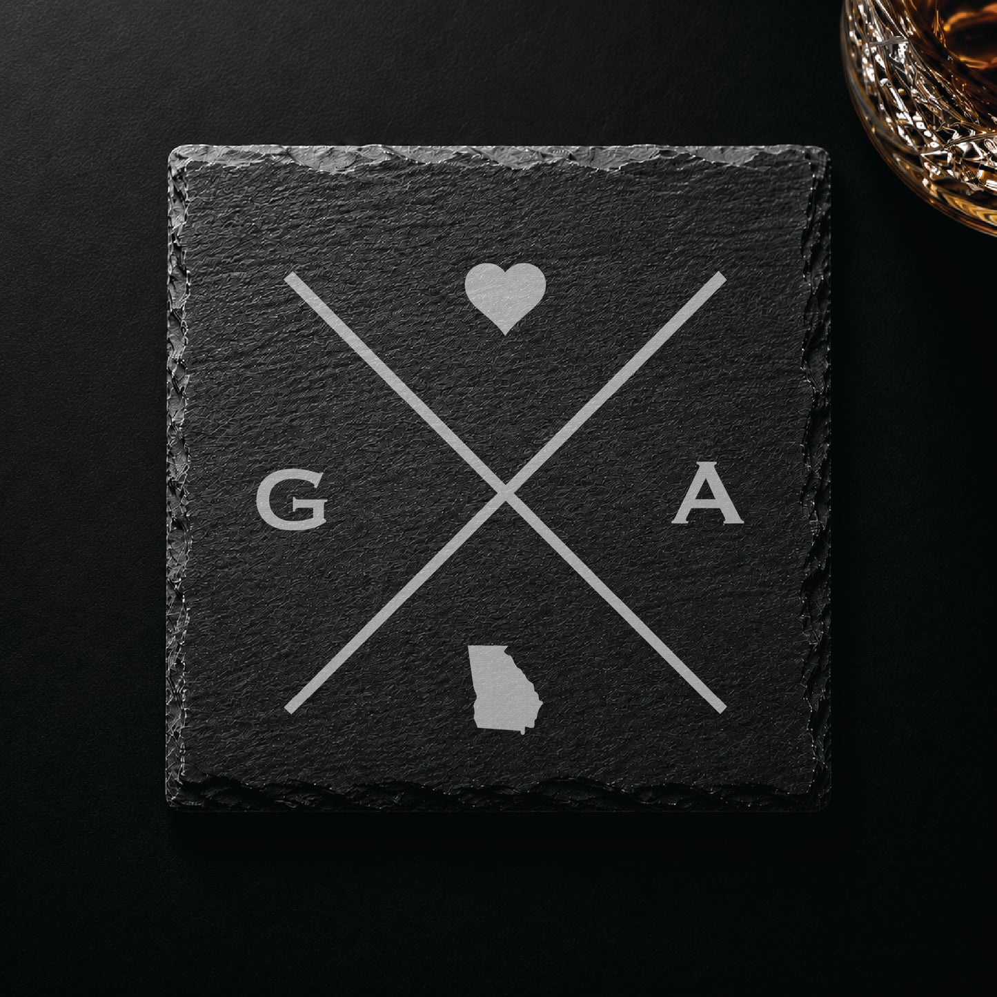 Dark slate coaster with engraved Georgia crossed-line design, heart icon, and Georgia silhouette on a dark background.