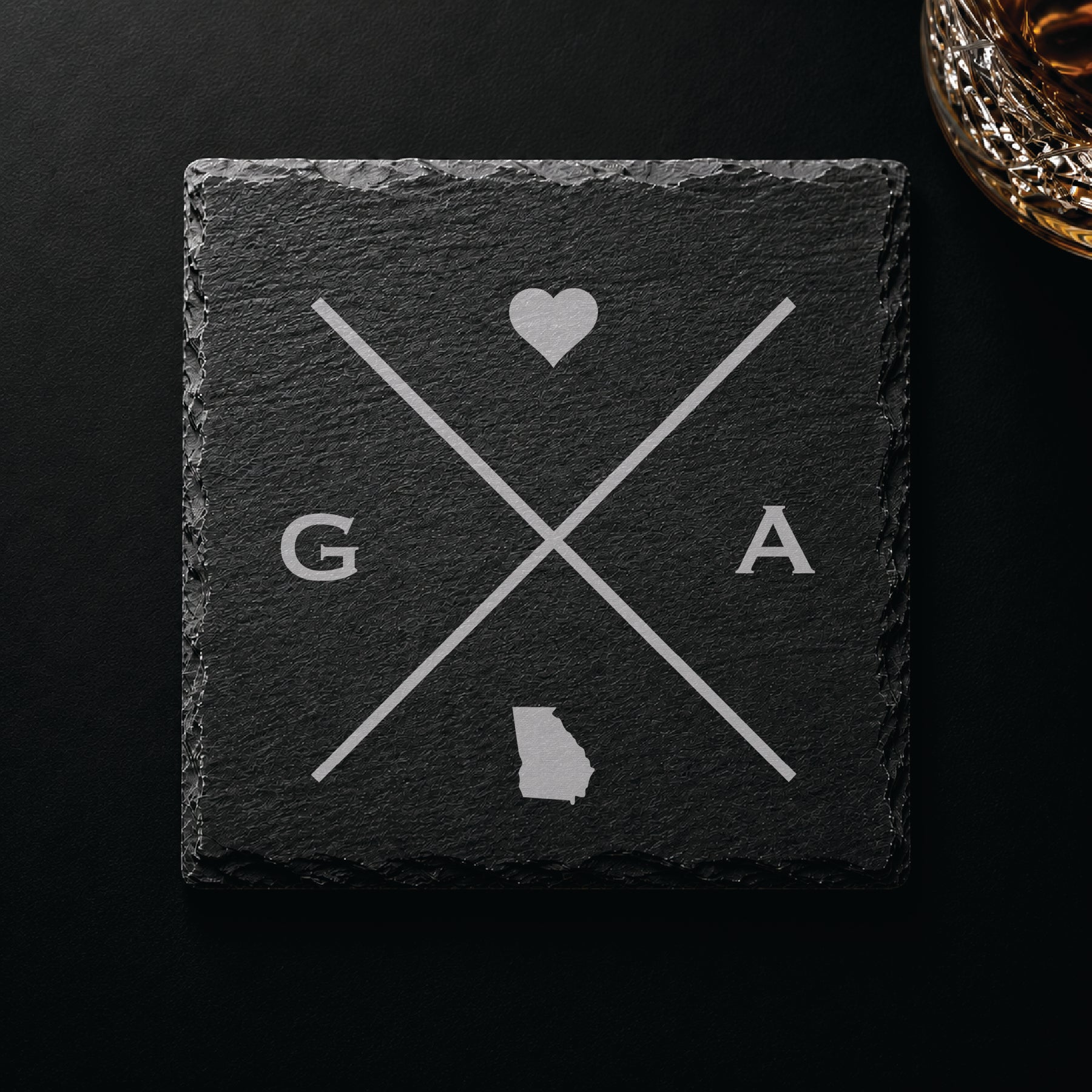 Dark slate coaster with engraved Georgia crossed-line design, heart icon, and Georgia silhouette on a dark background.