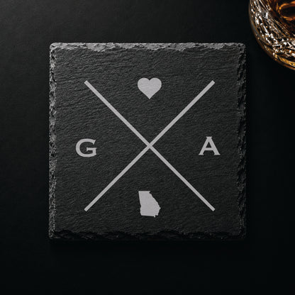 Dark slate coaster with engraved Georgia crossed-line design, heart icon, and Georgia silhouette on a dark background.