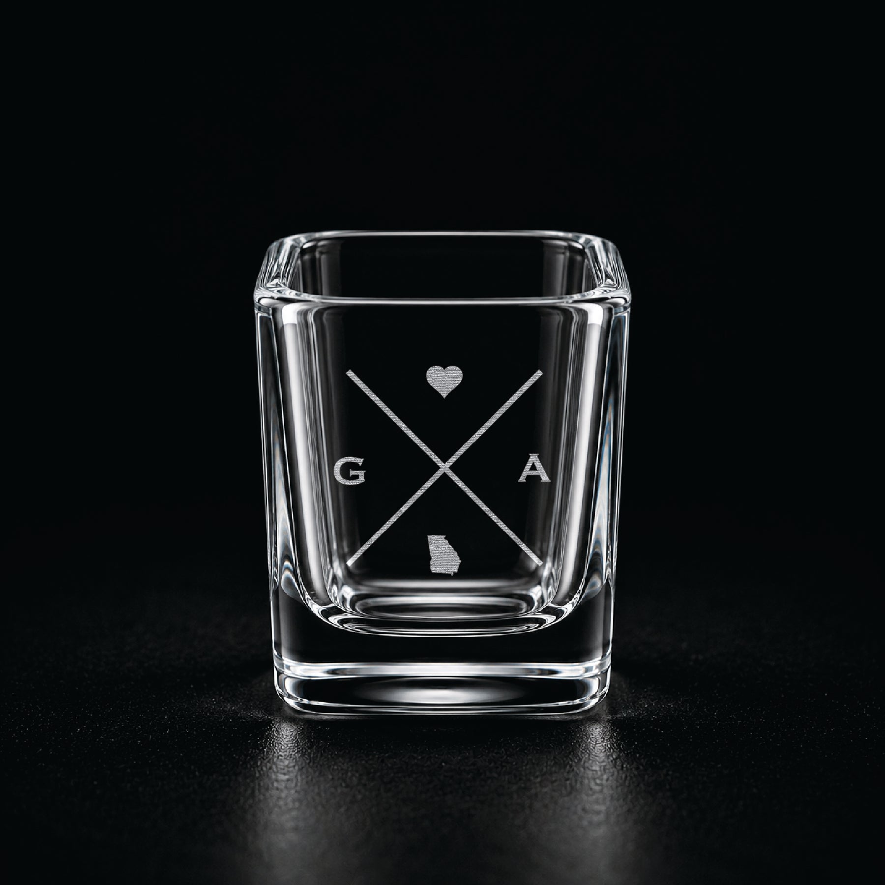 Engraved Georgia shot glass with modern crossed-line state design and frosted laser engraving on a dark background.