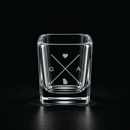 Engraved Georgia shot glass with modern crossed-line state design and frosted laser engraving on a dark background.