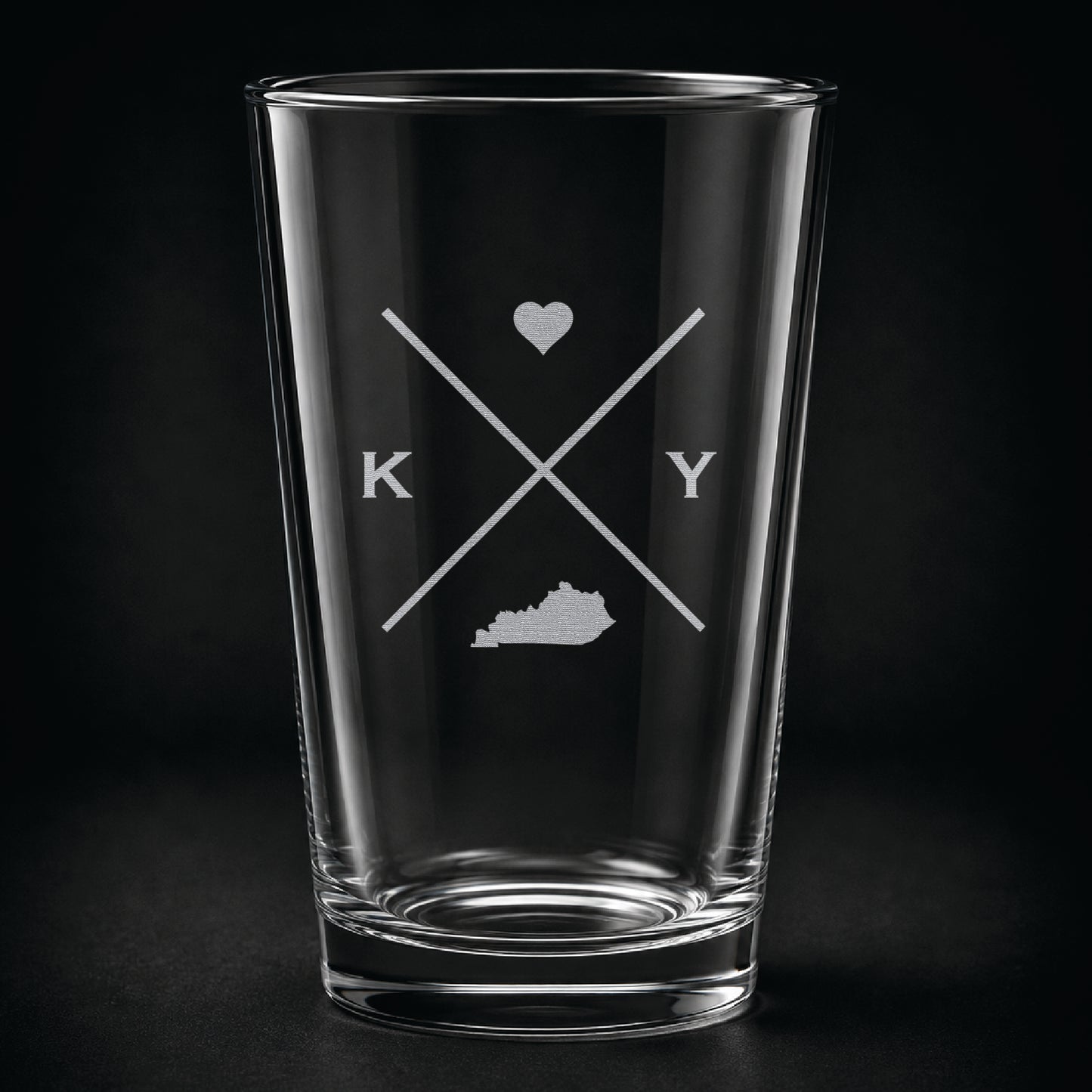 Engraved Kentucky pint glass featuring a minimalist crossed-line design with heart detail and Kentucky silhouette on a dark background.