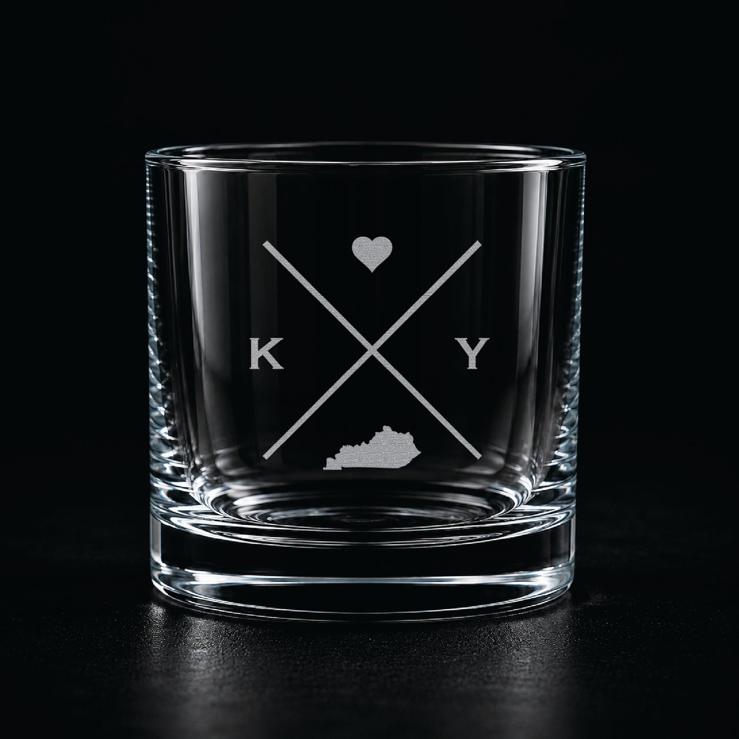 Engraved Kentucky rocks glass with frosted Kentucky silhouette and crossed-letter monogram on a dark background.