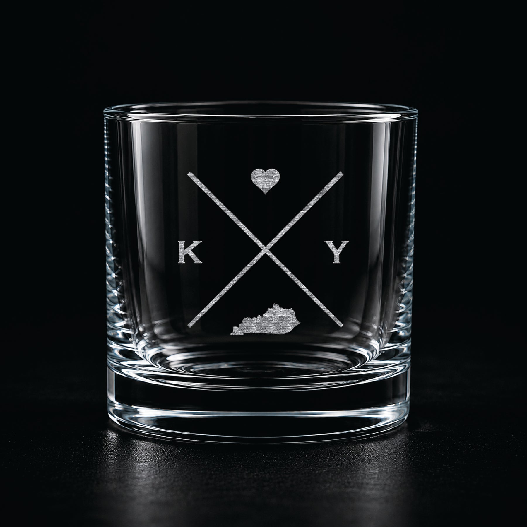 Engraved Kentucky rocks glass with frosted Kentucky silhouette and crossed-letter monogram on a dark background.