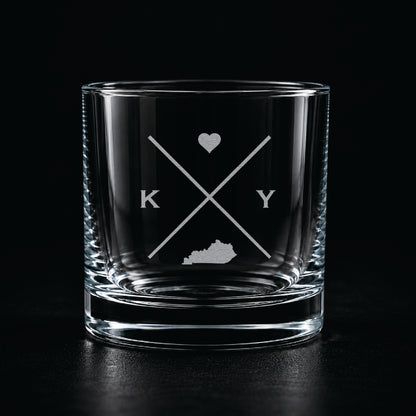 Engraved Kentucky rocks glass with frosted Kentucky silhouette and crossed-letter monogram on a dark background.