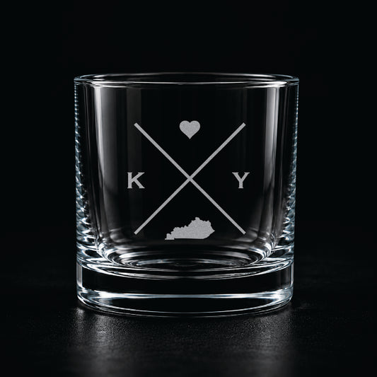 Engraved Kentucky rocks glass with frosted Kentucky silhouette and crossed-letter monogram on a dark background.