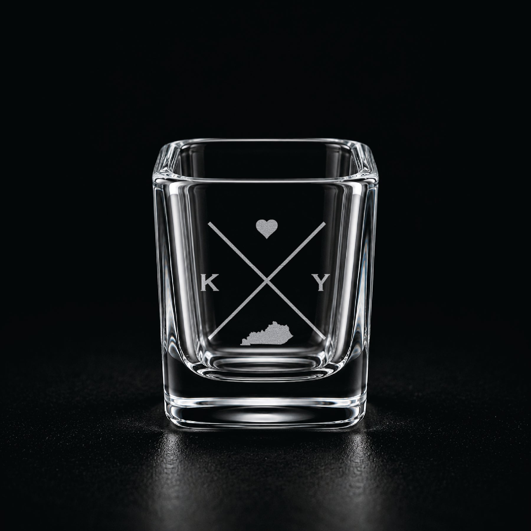 Engraved Kentucky shot glass with modern crossed-line state design and frosted laser engraving on a dark background.