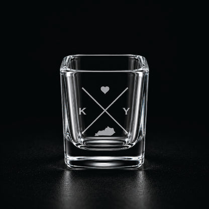 Engraved Kentucky shot glass with modern crossed-line state design and frosted laser engraving on a dark background.