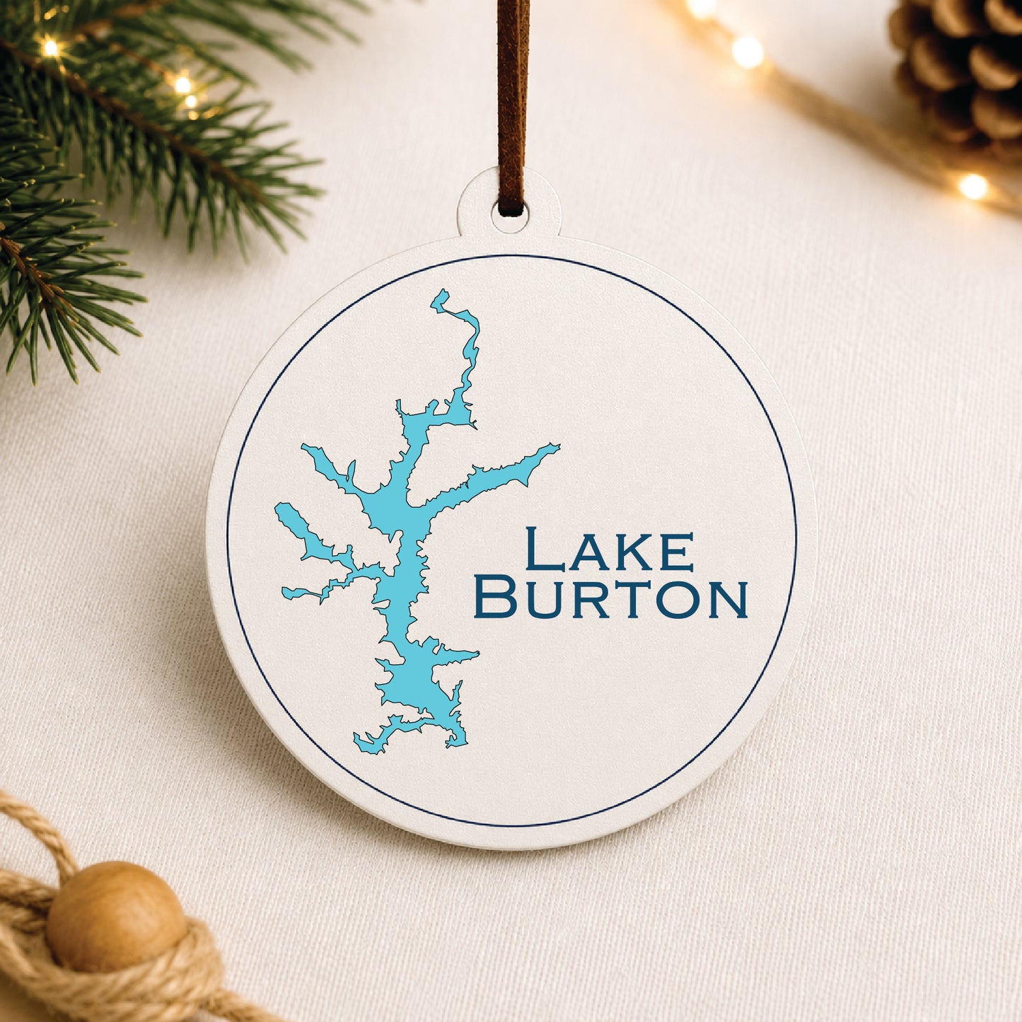 White Lake Burton ornament with blue lake map design on a warm holiday linen background with greenery and lights.