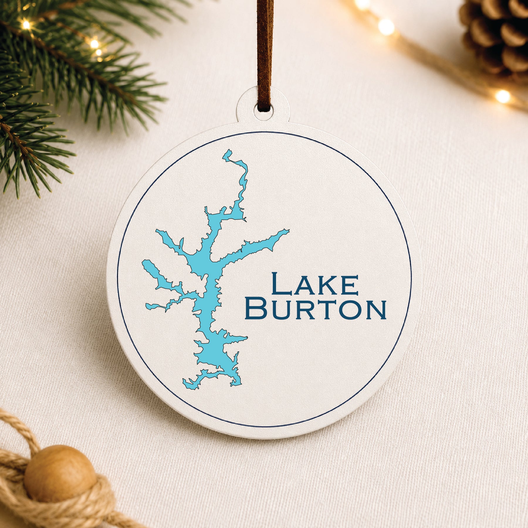 White Lake Burton ornament with blue lake map design on a warm holiday linen background with greenery and lights.
