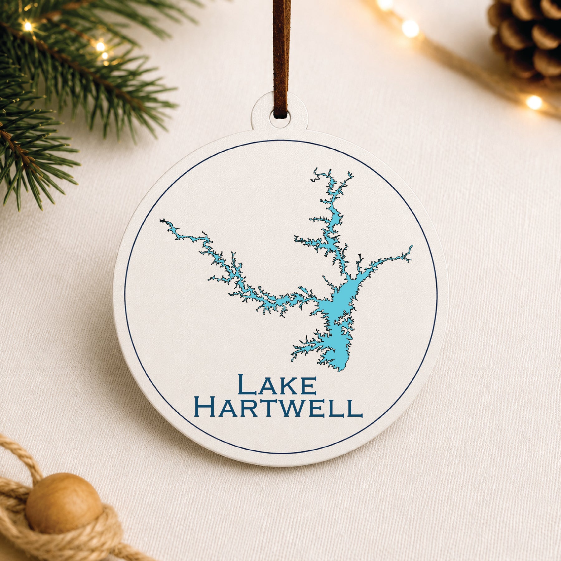 White Lake Hartwell ornament with blue lake map design on a warm holiday linen background with greenery and lights.