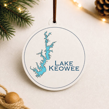 White Lake Keowee ornament with blue lake map design on a warm holiday linen background with greenery and lights.