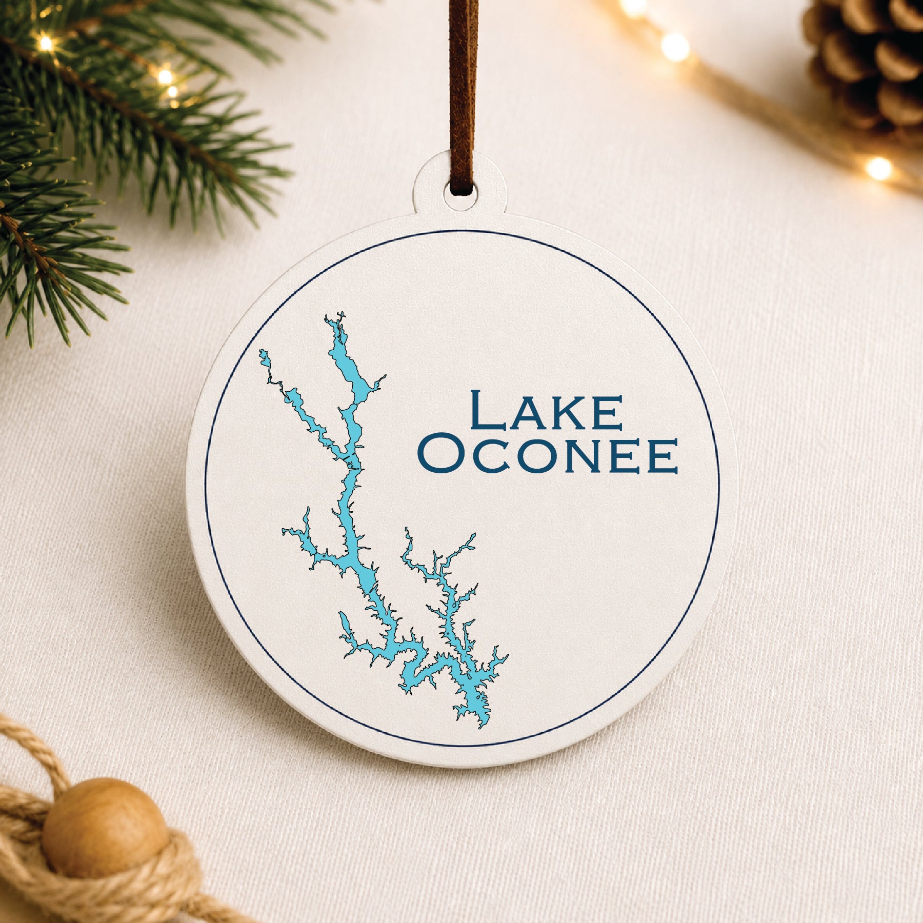 White Lake Oconee ornament with blue lake map design on a warm holiday linen background with greenery and lights.